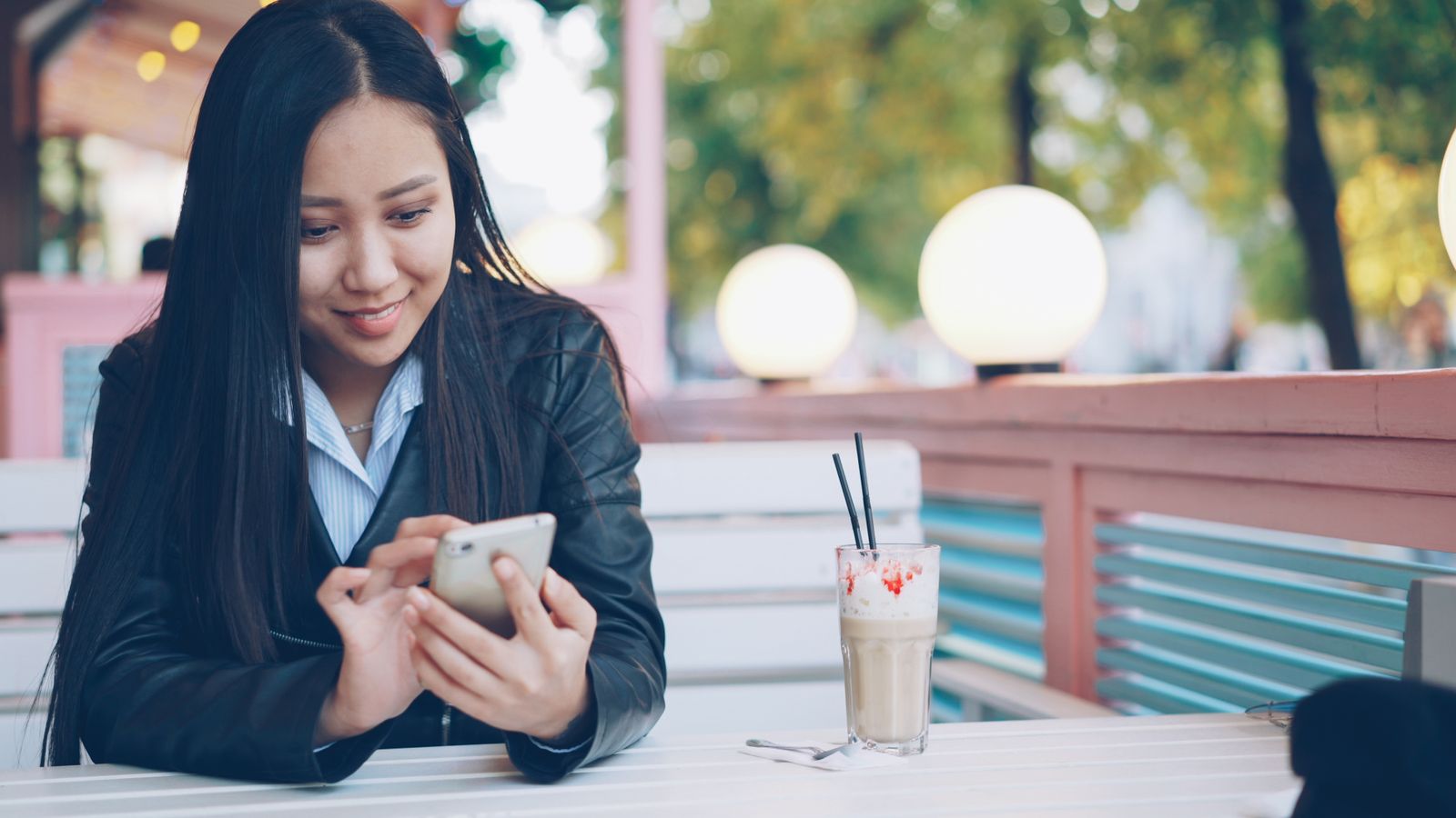 Cliente souriante consultant une notification sur son téléphone en terrasse de café