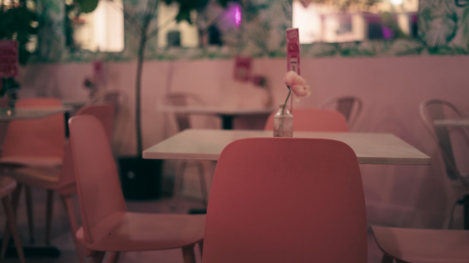 Café à l'ambiance rose avec une chaise vide au premier plan, évoquant un client absent
